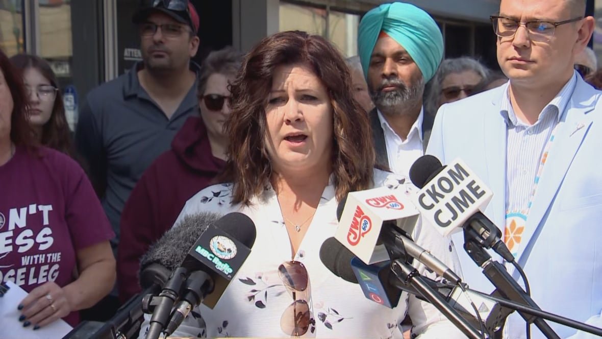 A woman in a black and white top speaks into microphones.