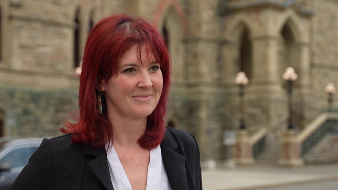 A woman with red hair standing in front of Parliament.
