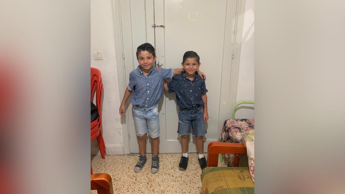 Two young boys in jean shorts and shirts smile at the camera.
