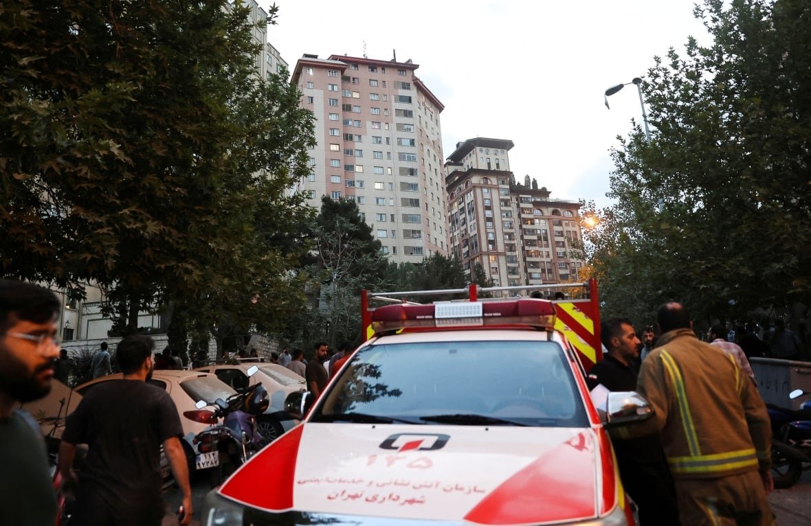 People gather on a Tehran street, near an emergency vehicle, in the aftermath of Israeli strikes.