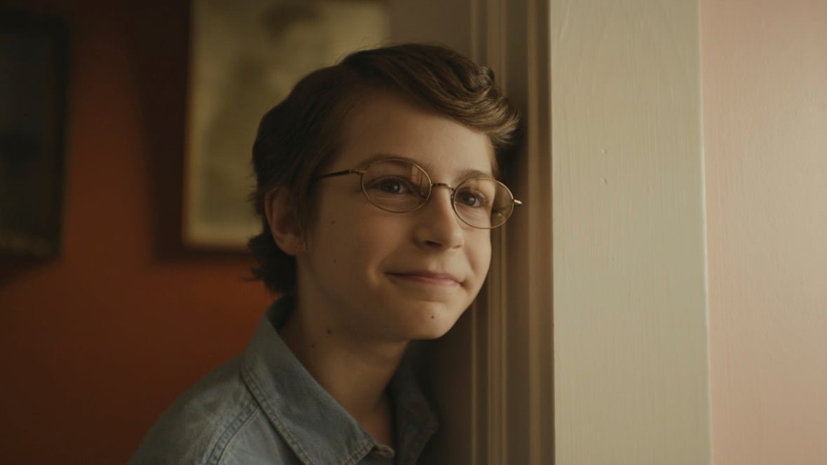 A smiling young boy leans against a door frame.