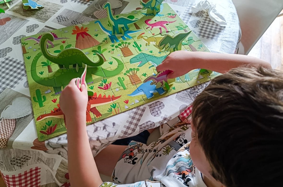 A boy plays with a dinosaur puzzle game on a table. 