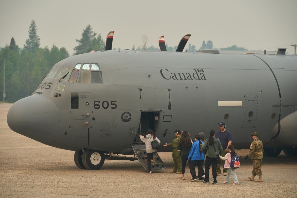 People board a large military aircraft as smoke fills the air around them. 