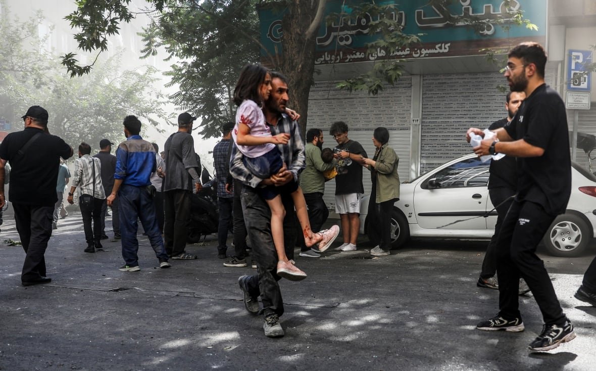 An adult carries a wounded child through a crowd.
