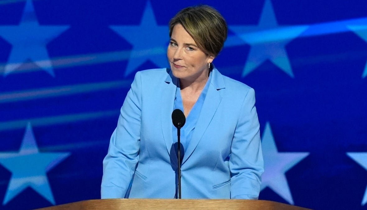 Maura Healey stands behind a microphone in front of a backdrop of stars. 
