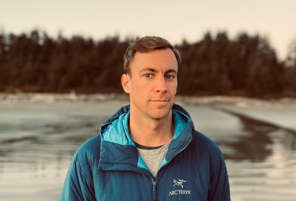 A man poses for a photo on a shoreline.