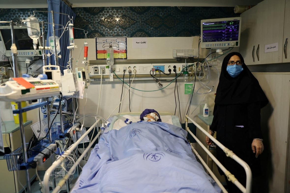 An injured child is seen in a hospital bed as an adult stand beside them.