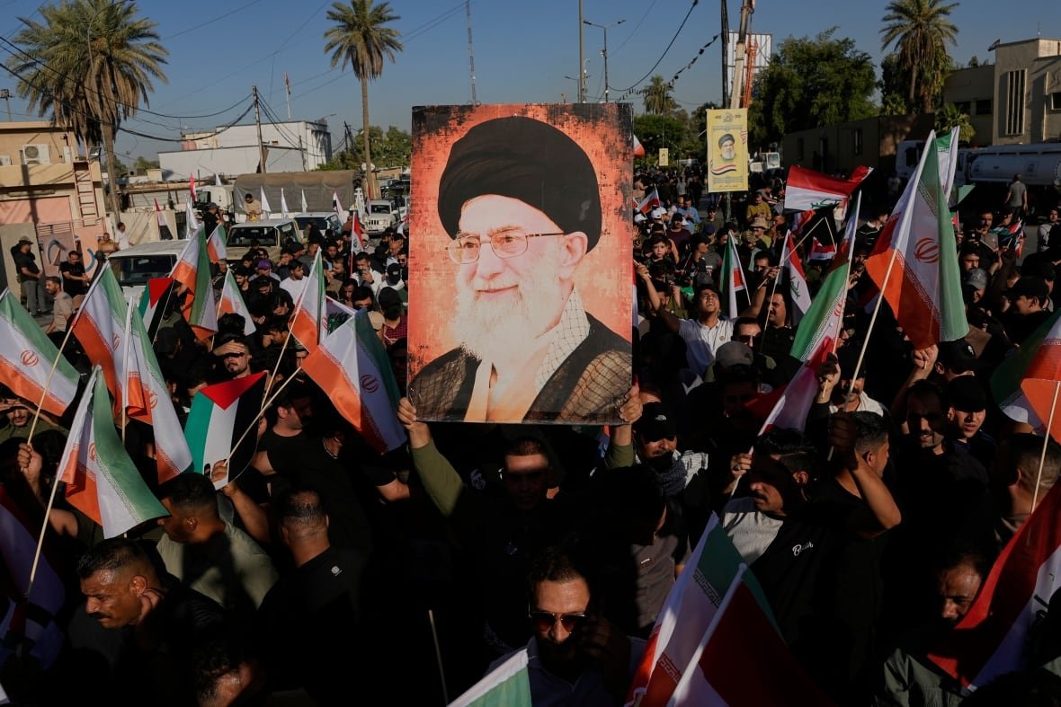 Demonstrators hold up flags and a sign featuring a person's portrait during an outdoor rally.