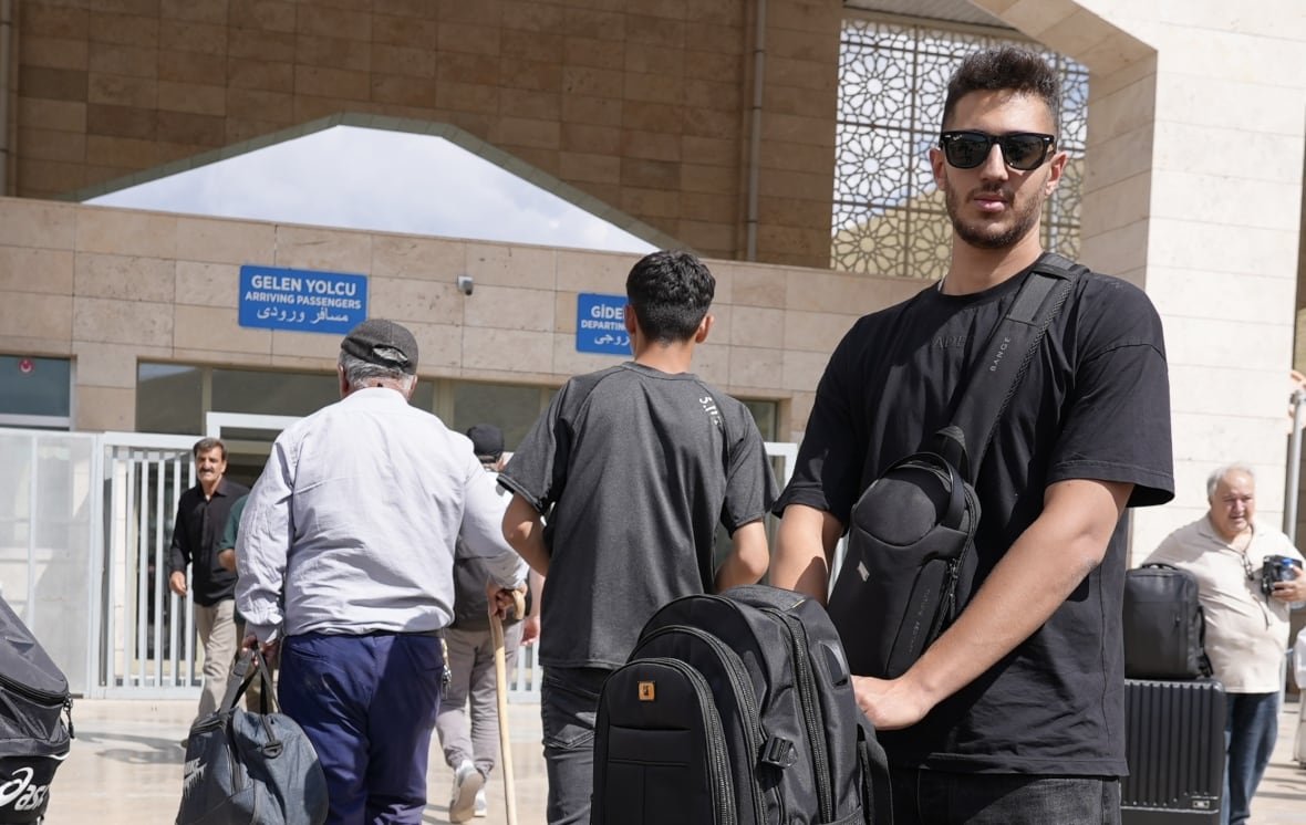 A man wearing sunglasses stands with luggage in front of him. 