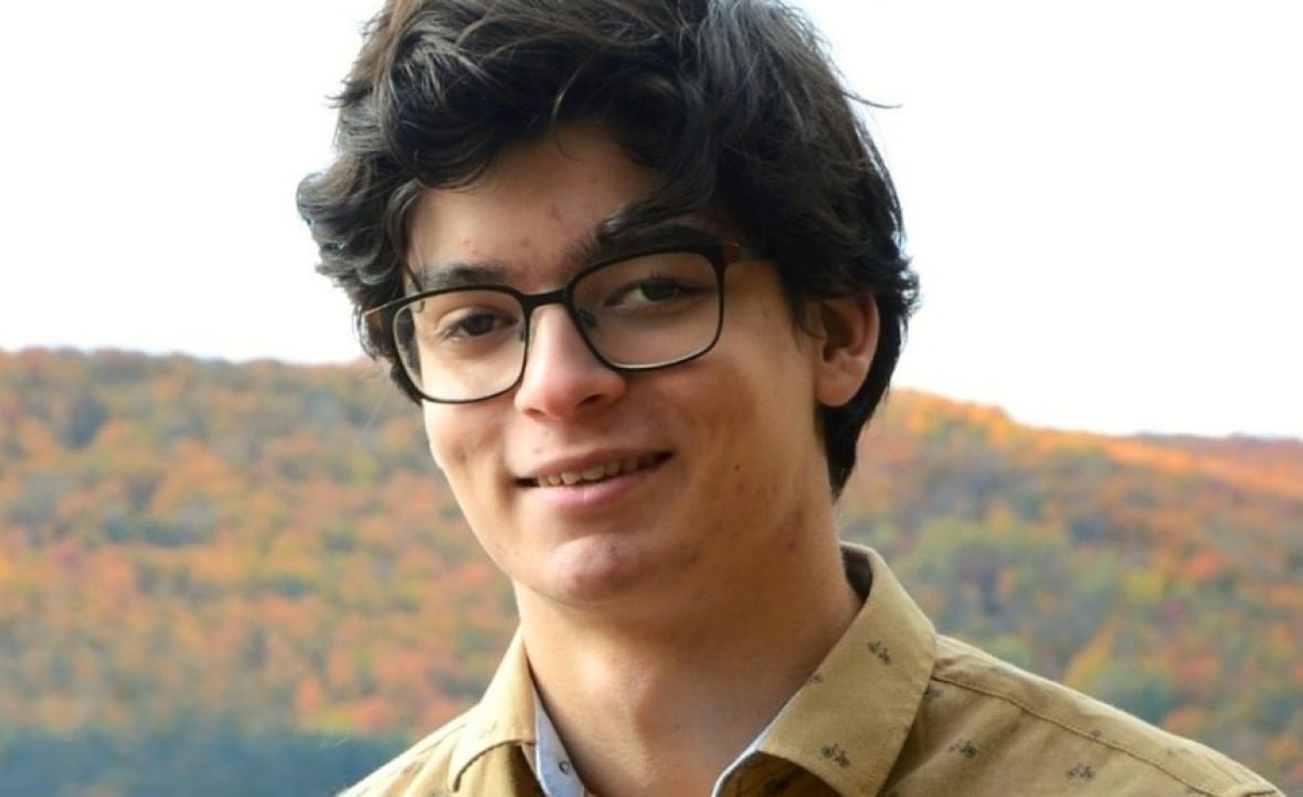 A man with glasses in front of a mountain covered in colourful trees.