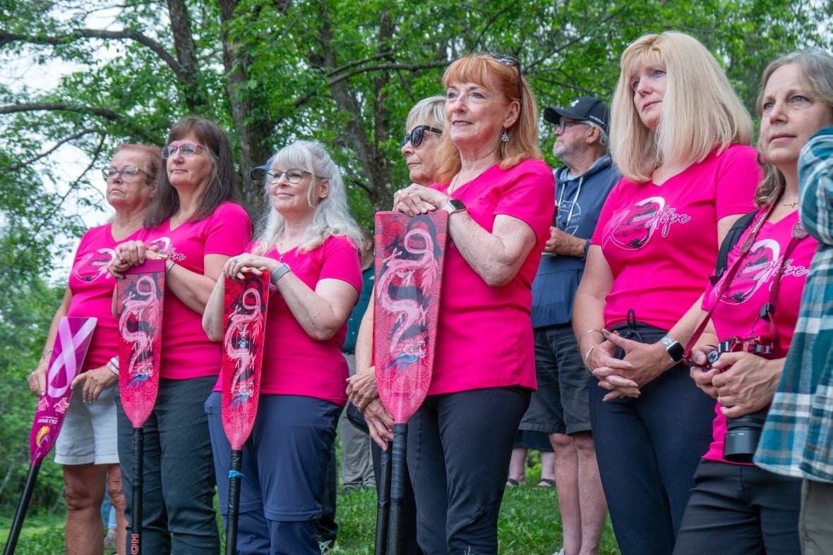 A group of people wearing pink shirts is seen standing outside, holding pink paddles.