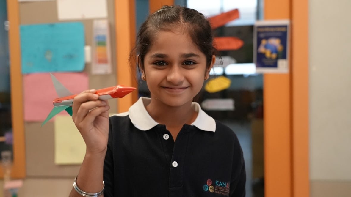 A smiling young girl holds up a small rocket.