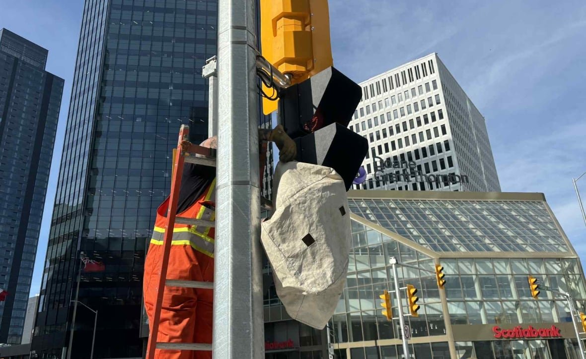 A construction work in orange coveralls removes the cover off of a traffic signal.