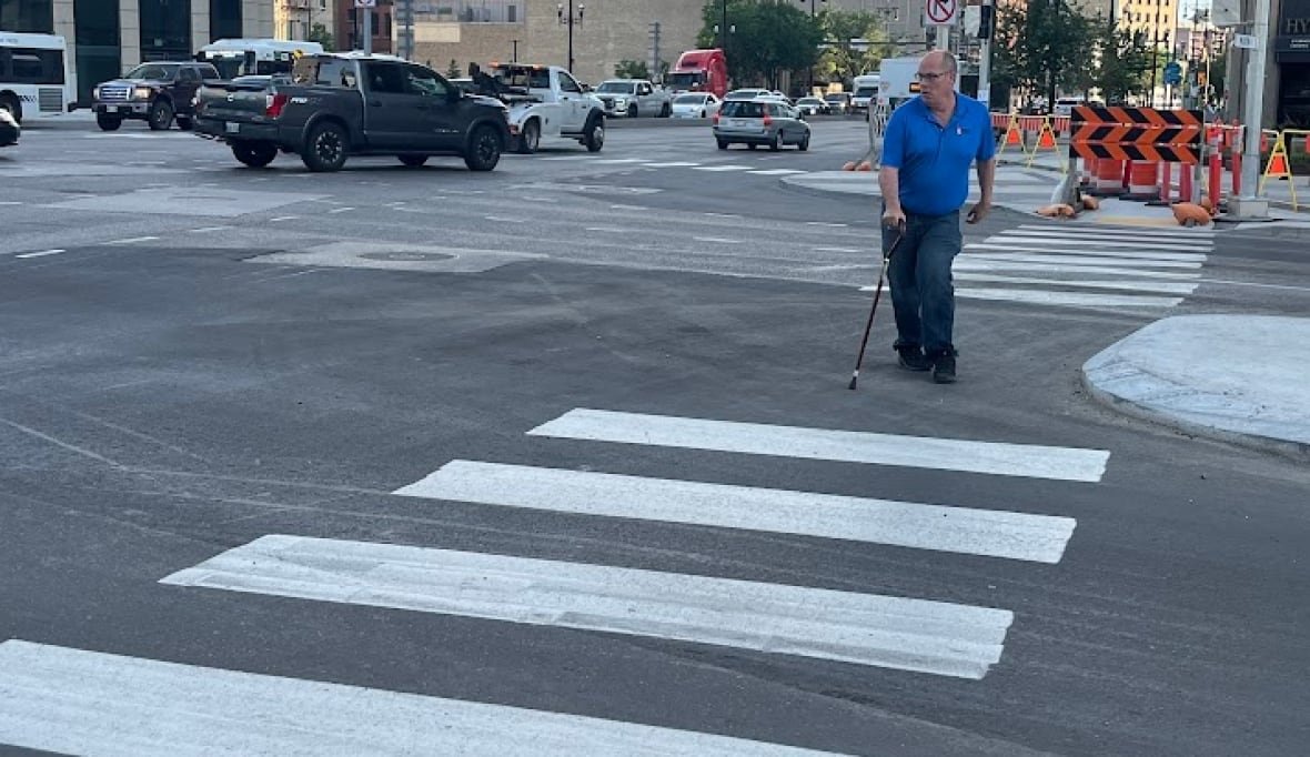 A man with a cane walks through a street crosswalk.