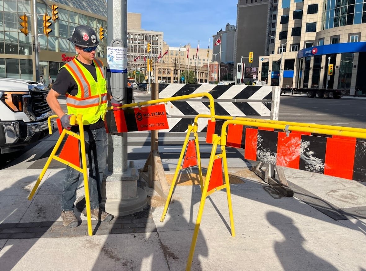 A construction worker in bright colours removed metal barricades near a street corner.