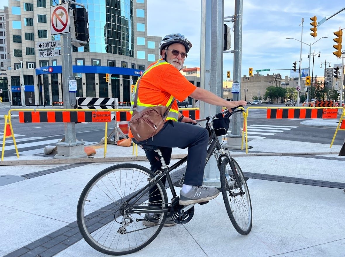 A man with a white beard sits on a bike at a street corner