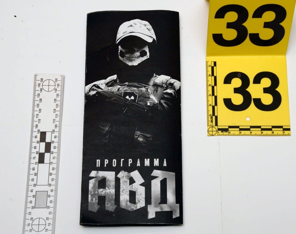 A black and white core of a pamphlet showing a man in a skull mask with a firearm and words in Russian.