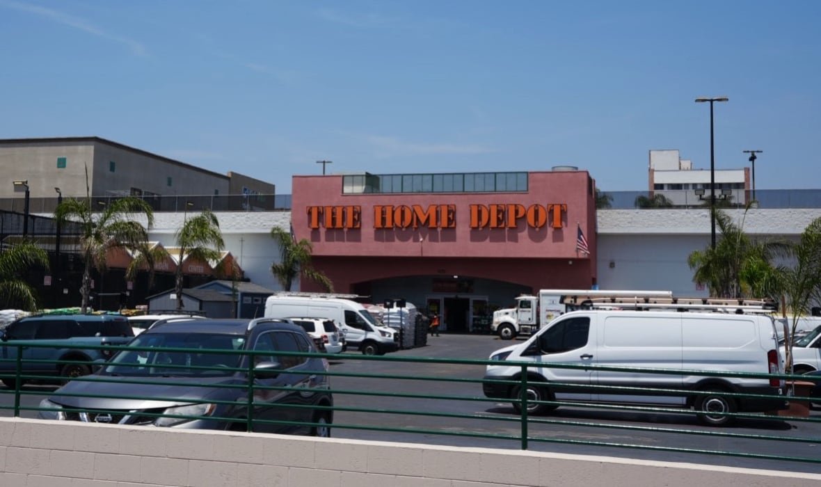 A Home Depot building and parking lot full of cars under a blue sky. 