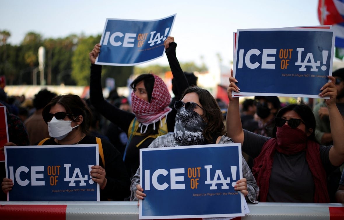 Protesters wearing face coverings hold up signs that read, 'ICE out of LA.'