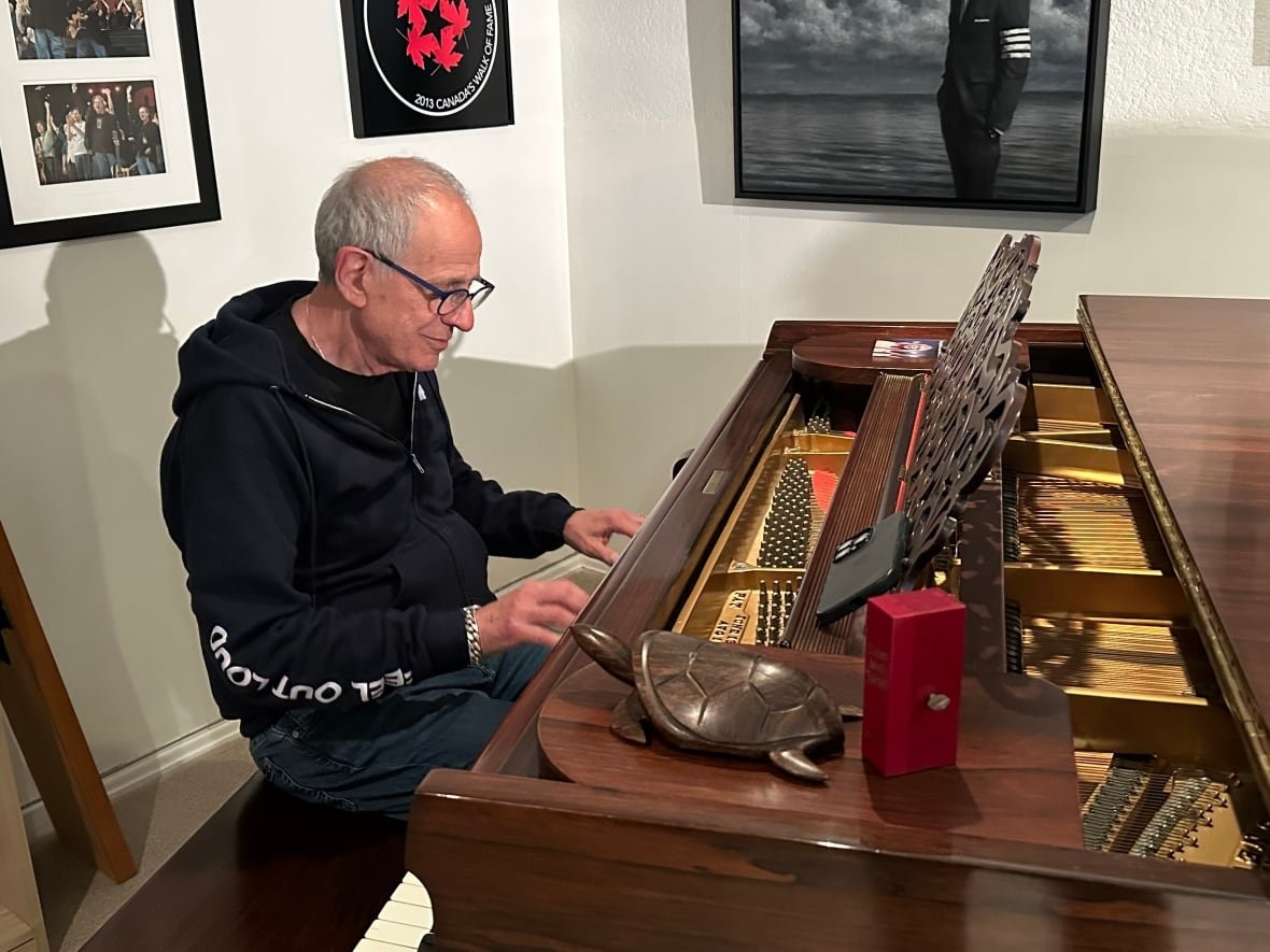 A man in a black sweater plays a large brown piano.