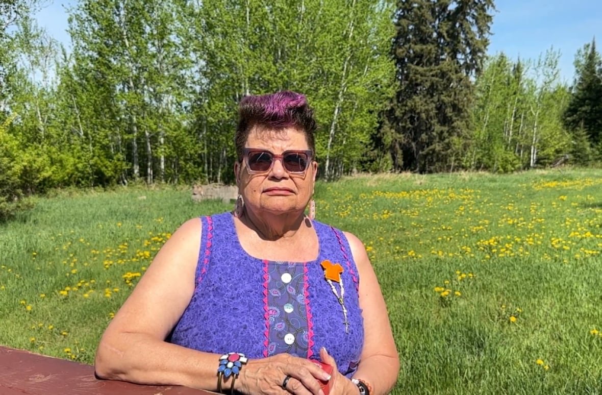 A woman in a purple dress sits on the grounds where the residential school once stood. 