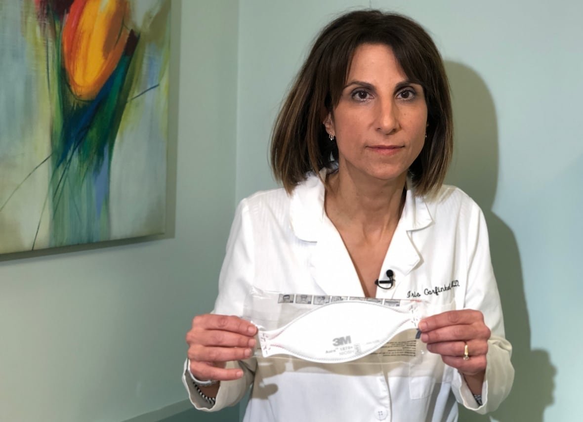 A doctor in a white coat holds up an N-95 mask.