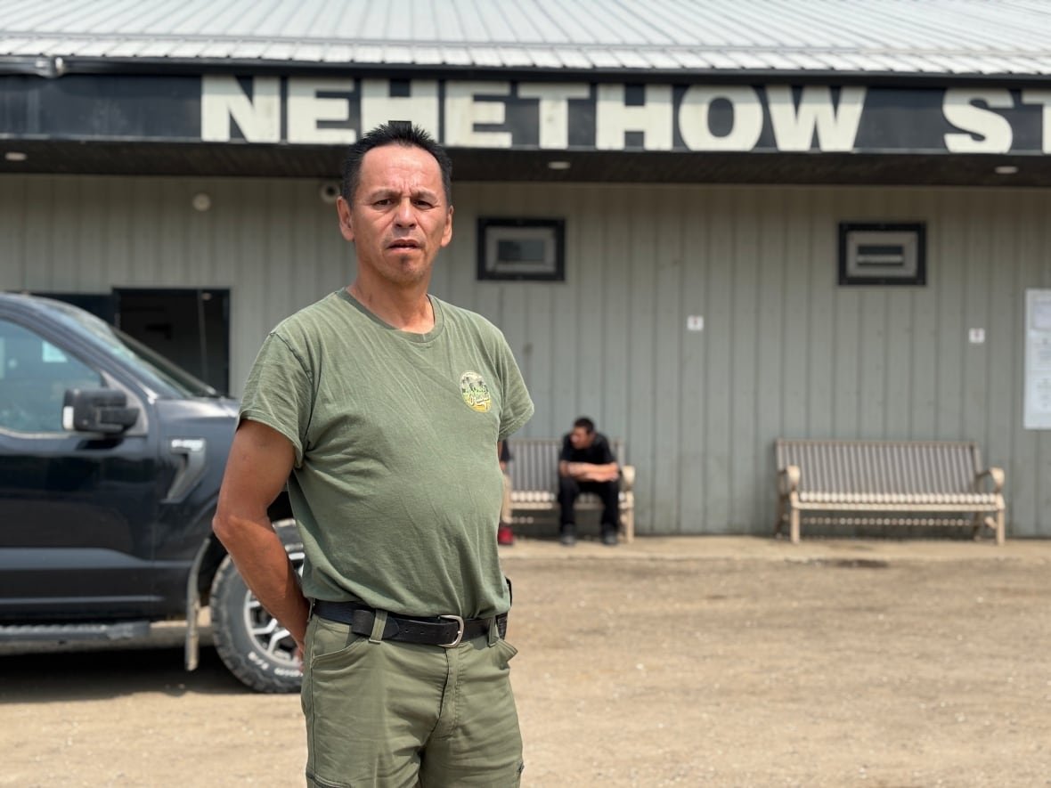 A man in a khaki shirt and khaki pants stands in front of a building.