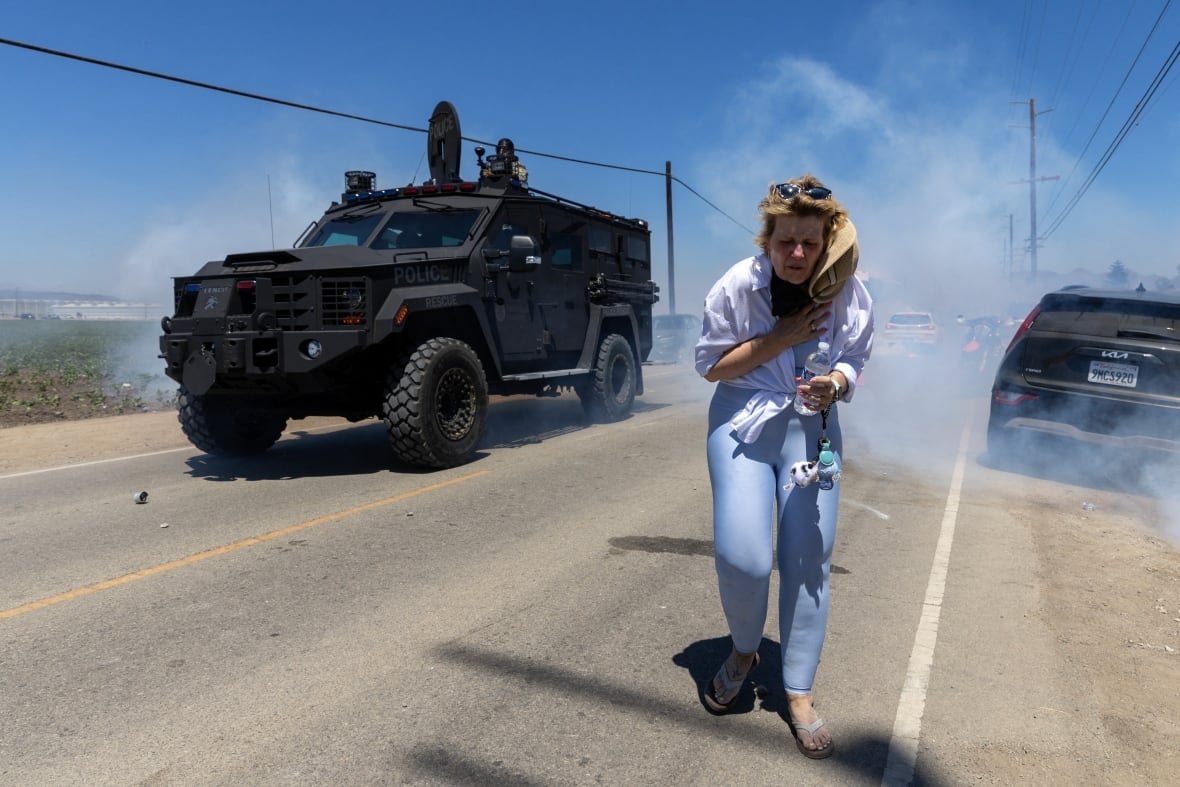 A protester flees from tear gas and armored personnel vehicles.