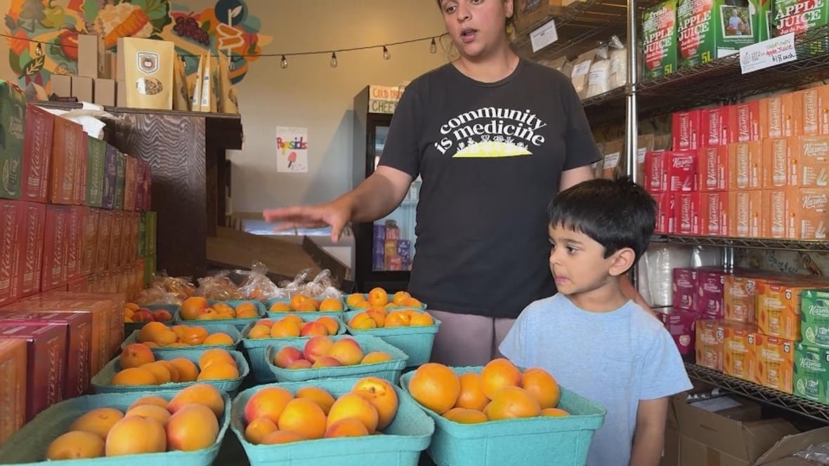A woman points to buckets of peaches as a boy looks on.