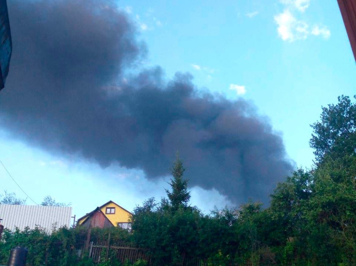 Large clouds of grey and black smoke are shown in a bright blue sky above what appears to be a residential structure.