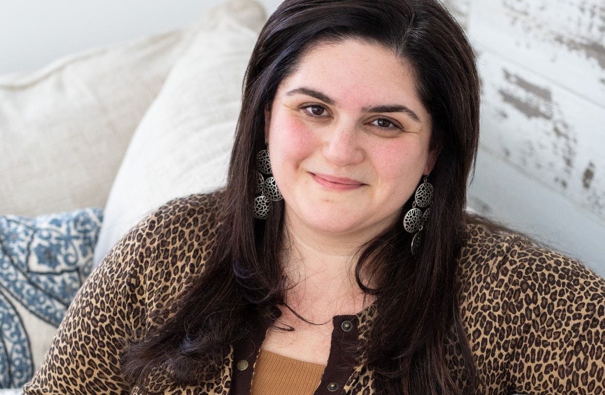 A woman sits on a sofa, smiling for the camera