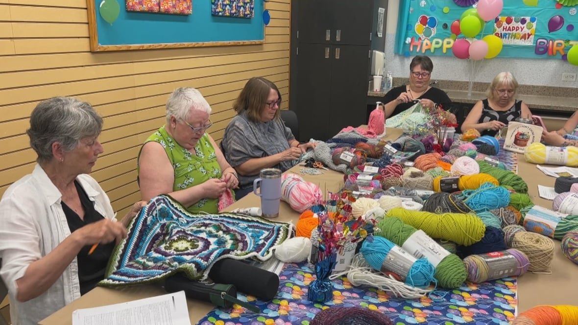 A group of women sit around a table full of yarn working on projects.