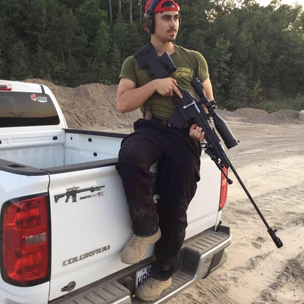 A man sitting on the back of a pickup truck holding a firearm.