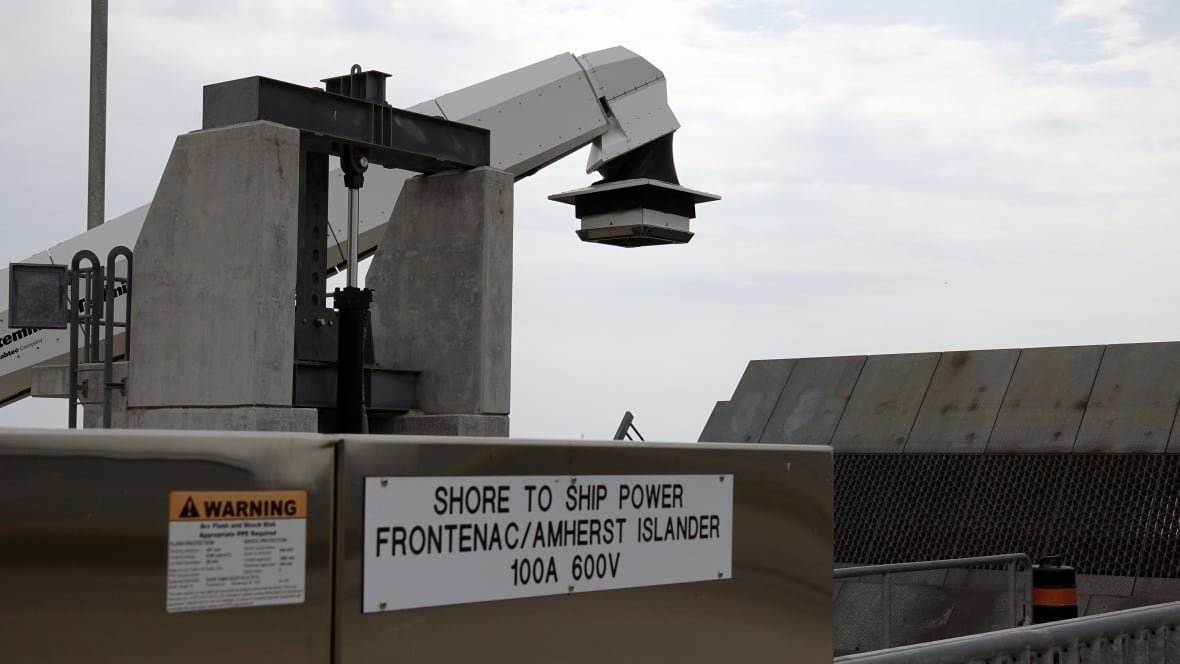 A closeup photo of a metal cabinet with the words "Shore to Ship Power" on it. A large metal ramp cars use to enter and exit the ferry can be seen in the background.