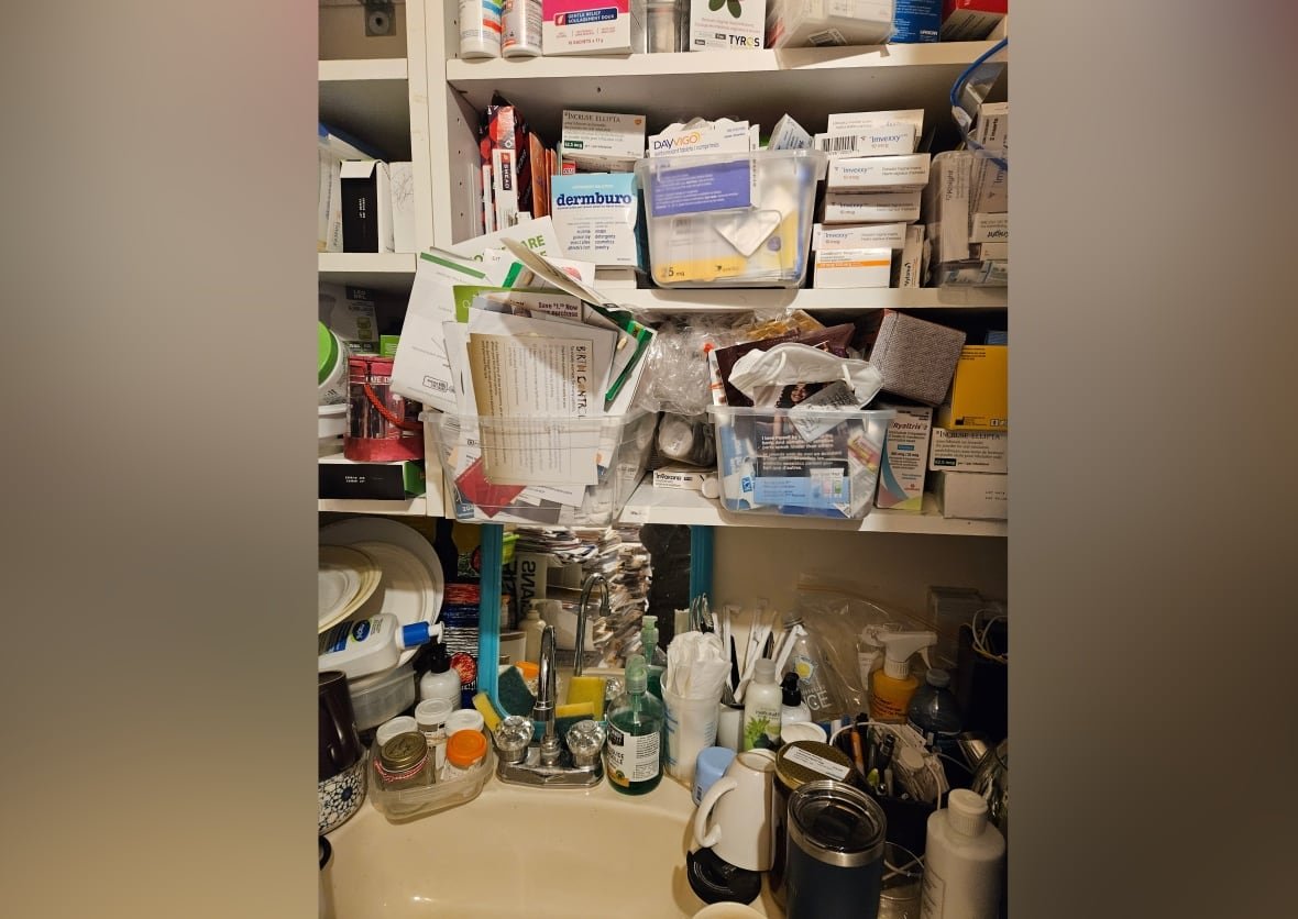A sink surrounded by documents, a coffee mug, specimen jars, drug samples, lotion jars, piled on top of each other.