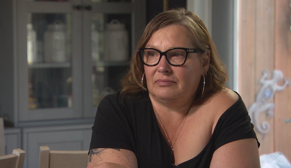 A woman with short brown hair, wearing black eyeglasses and a black short sleeved shirt, looks off side.
