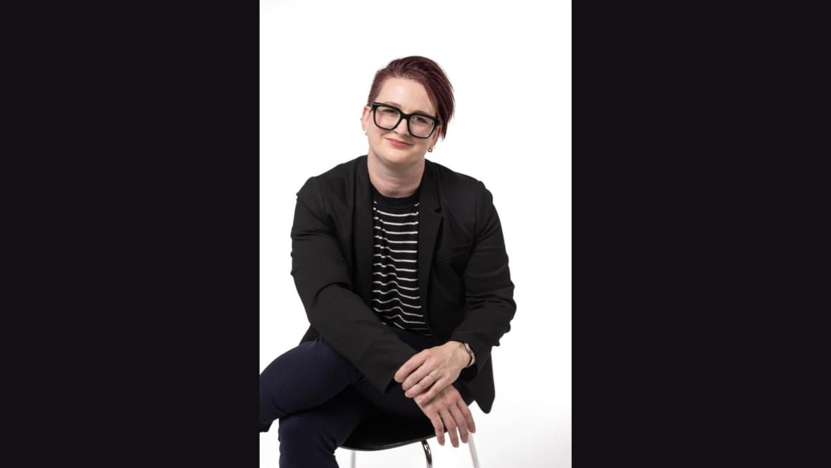 A person with short hair and glasses is seen sitting on a chair.