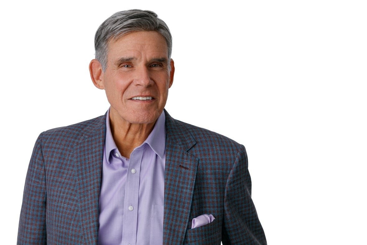 A man in a sports jacket and pocket square smiles at the camera