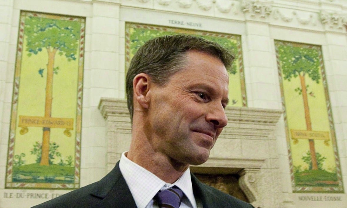 A man stands in front of a mantle decorated with art.