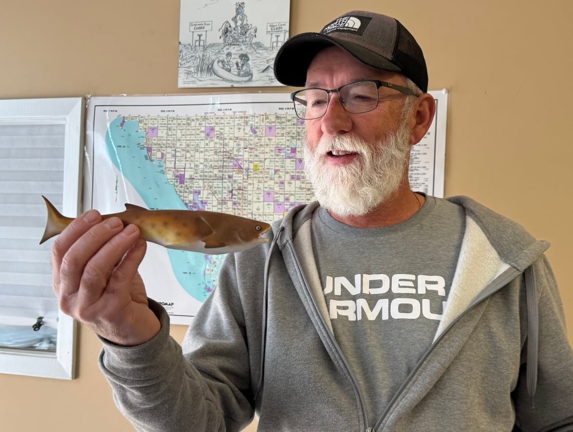 A man holds a model of a fish in one hand.