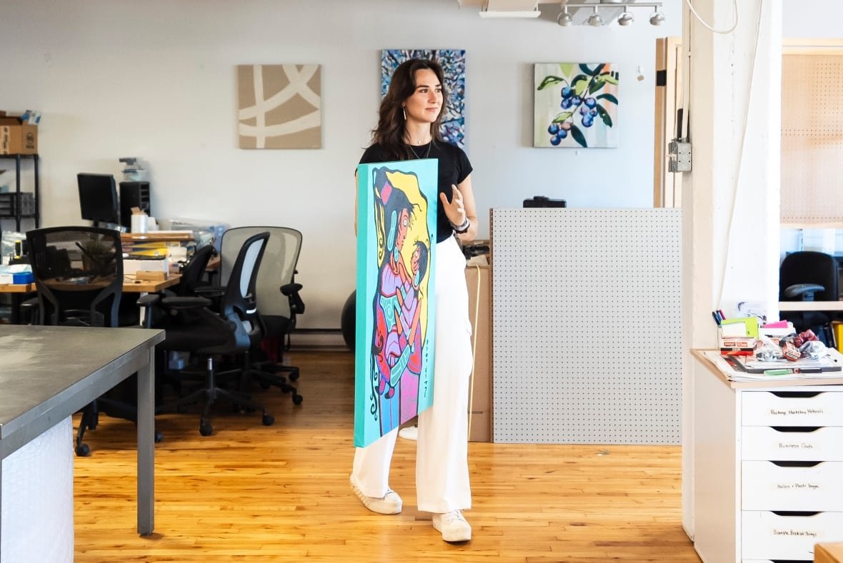 A woman holds up a painting.