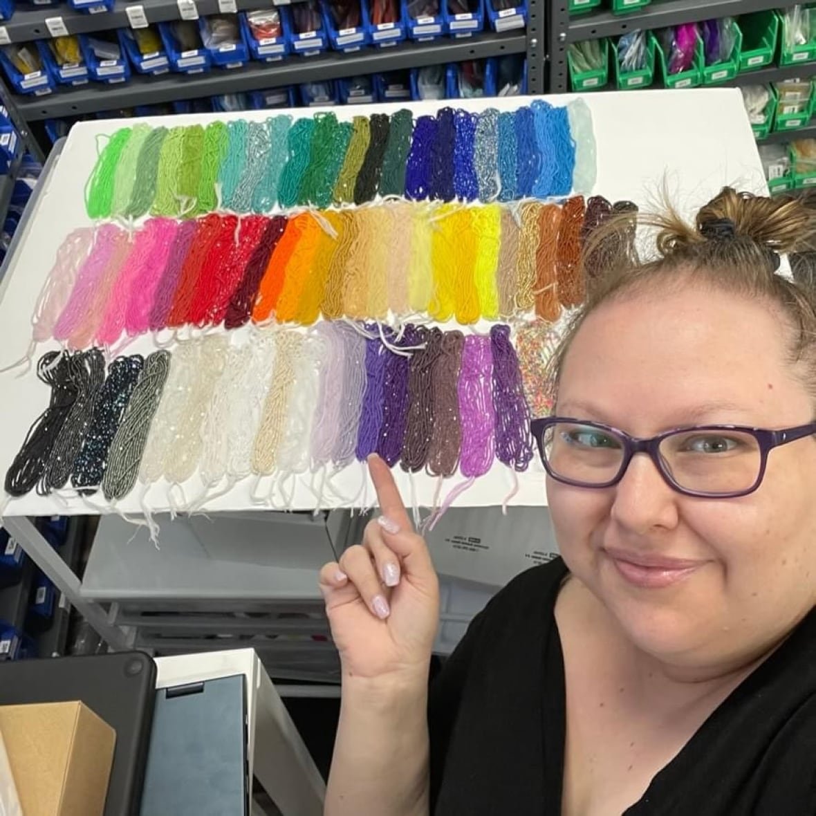 A close up of a woman pointing at strands of colourful beads sitting on a table behind her. 