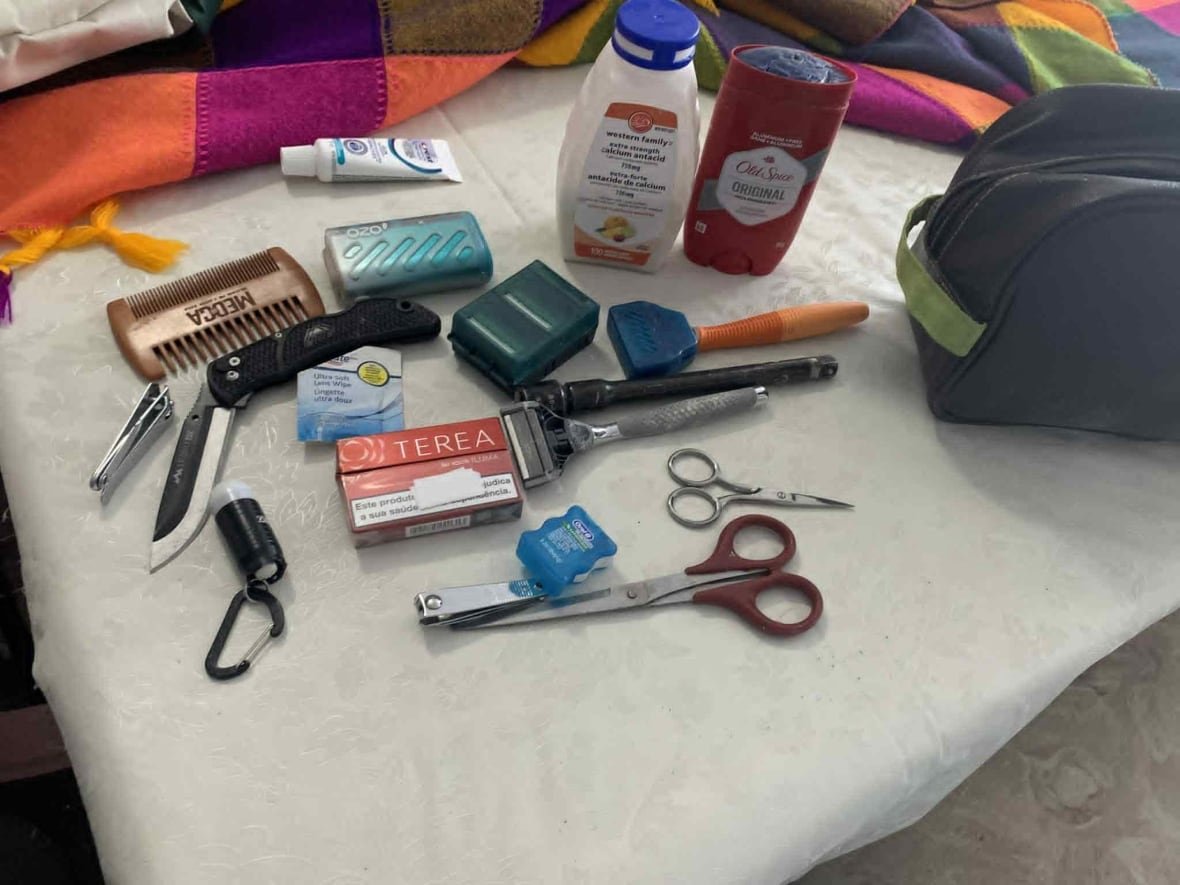 A small black back with items laid out, like a comb, nail clippers, tooth floss, scissors, body wasg, razors and a knife.