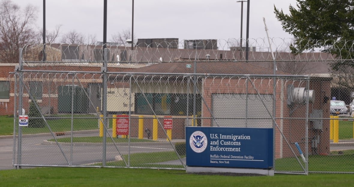 A sign that reads Immigration and Customs Enforcement, Buffalo field division, Batavia, NY. Behind the sing is a chain link fence topped with concertina wire.