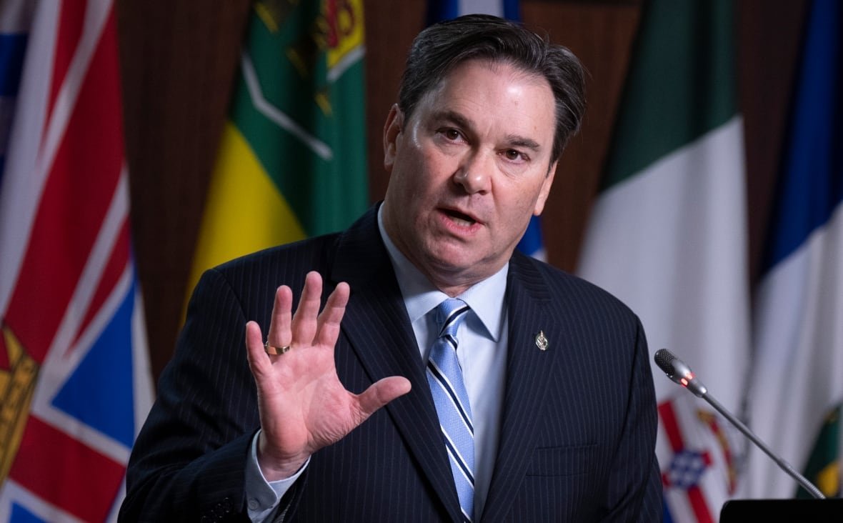 A man gestures with his hand as he speaks into a microphone.