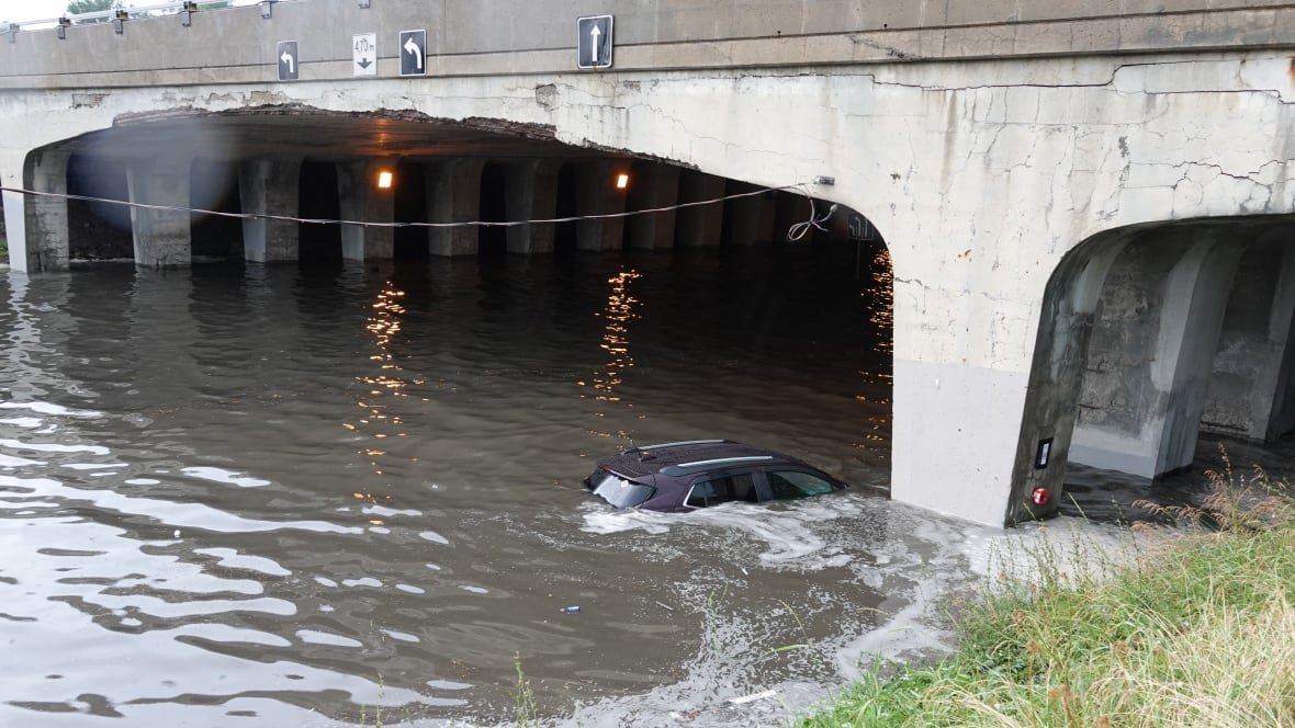 Water sits halfway up the windows of a vehicle stuck under a flooded underpass.