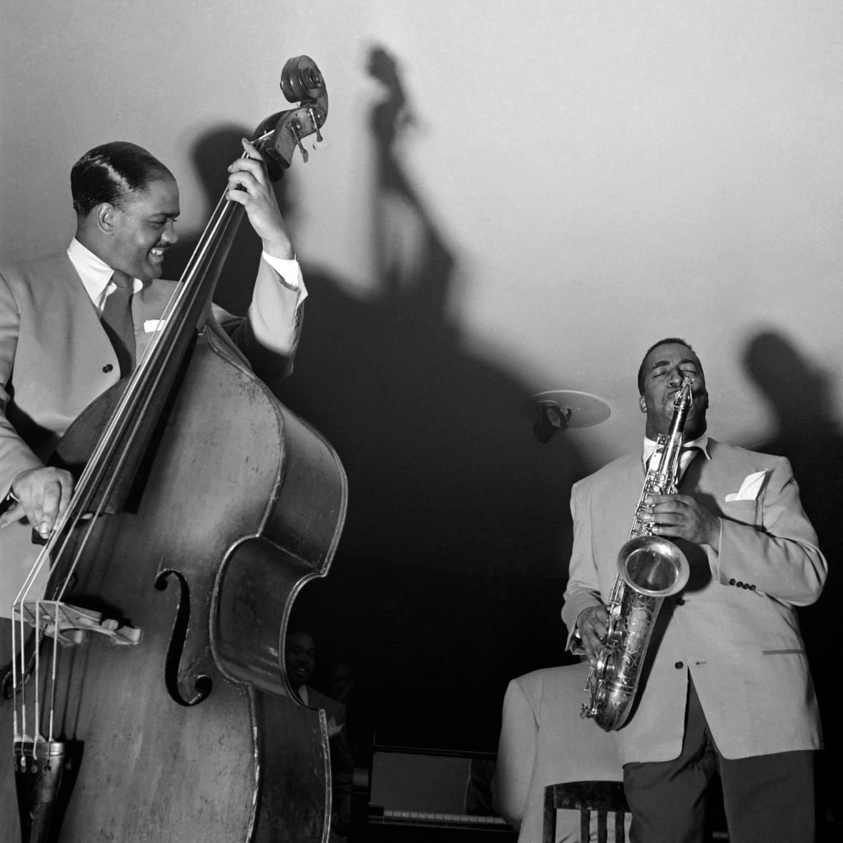 Black and white image of two bBack men in suits, one on saxophone and one on stand-up bass, jamming together
