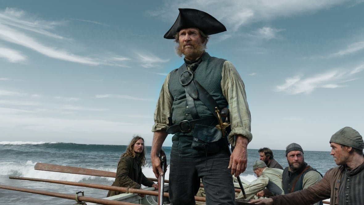 A man standing in a ship wearing  a naval outfit is shown.