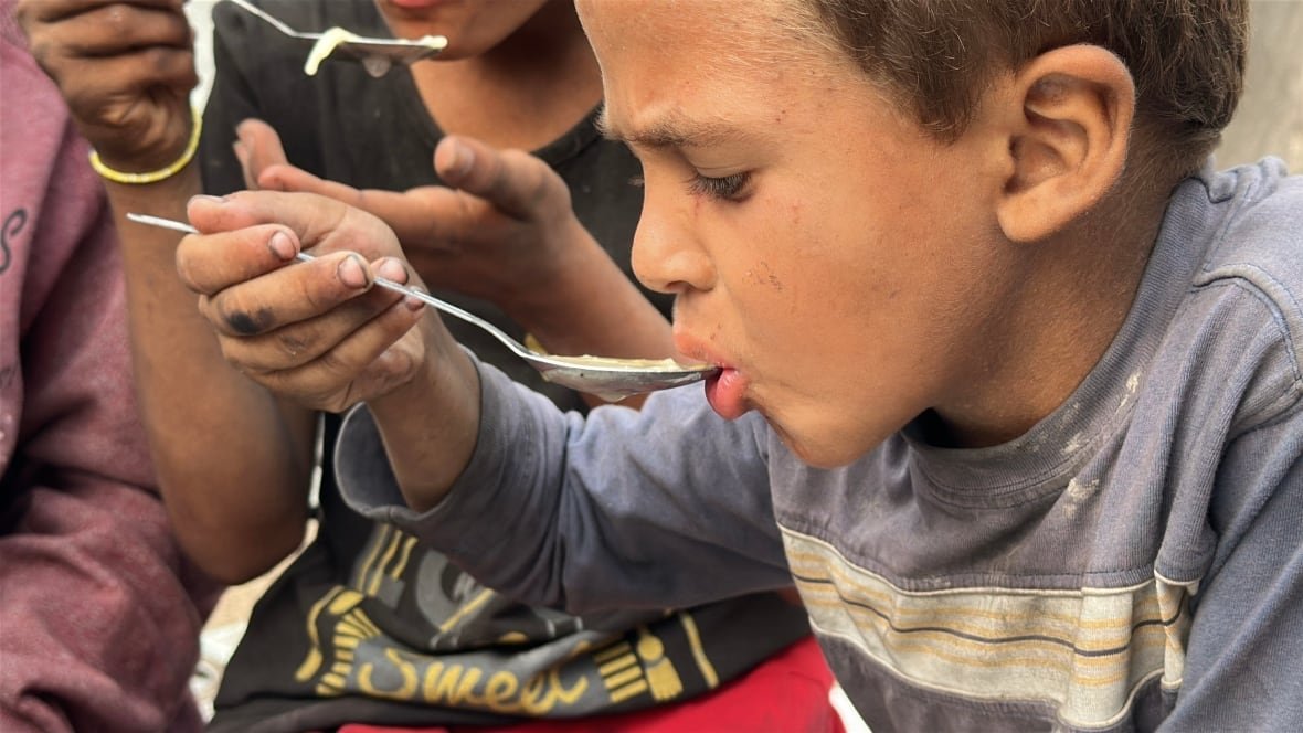A young boy brings a spoon of noodles to his mouth.
