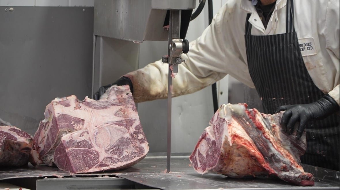 A butcher guides a huge piece of beef through a meat saw inside a butchery